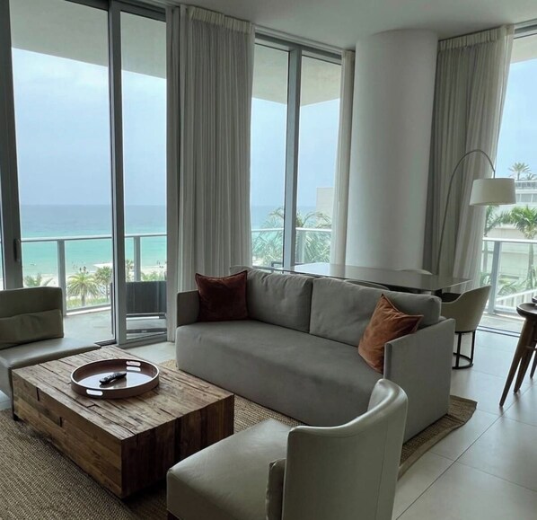 A modern living room with a large sofa, a coffee table, and a view of the ocean.