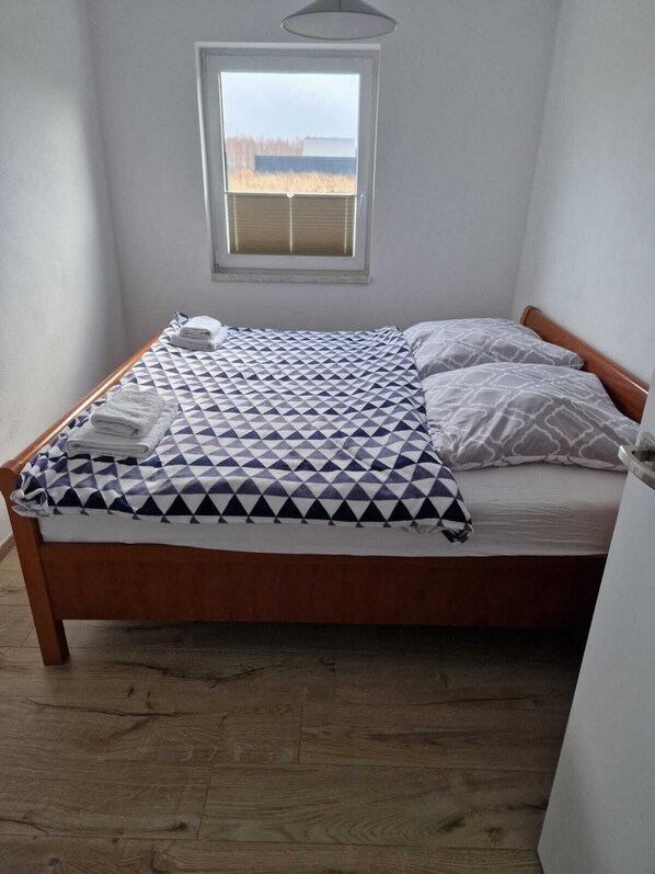 Una cama individual con una colcha de estampado geométrico, un cabecero de madera y una ventana con persianas.
