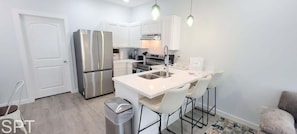 Una cocina moderna con armarios blancos, electrodomésticos de acero inoxidable y una isla central con taburetes de bar.