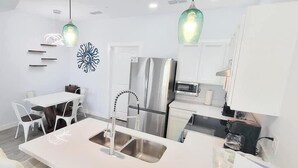 A modern kitchen with white cabinetry, a stainless steel refrigerator, and pendant lighting. - Villas De Laguna 1 3 Bedroom Home (South Padre Island)
