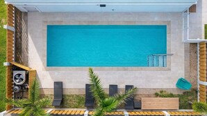 A rectangular swimming pool with a tiled deck, surrounded by a wooden deck and palm trees. - Villas De Laguna 1 3 Bedroom Home (South Padre Island)