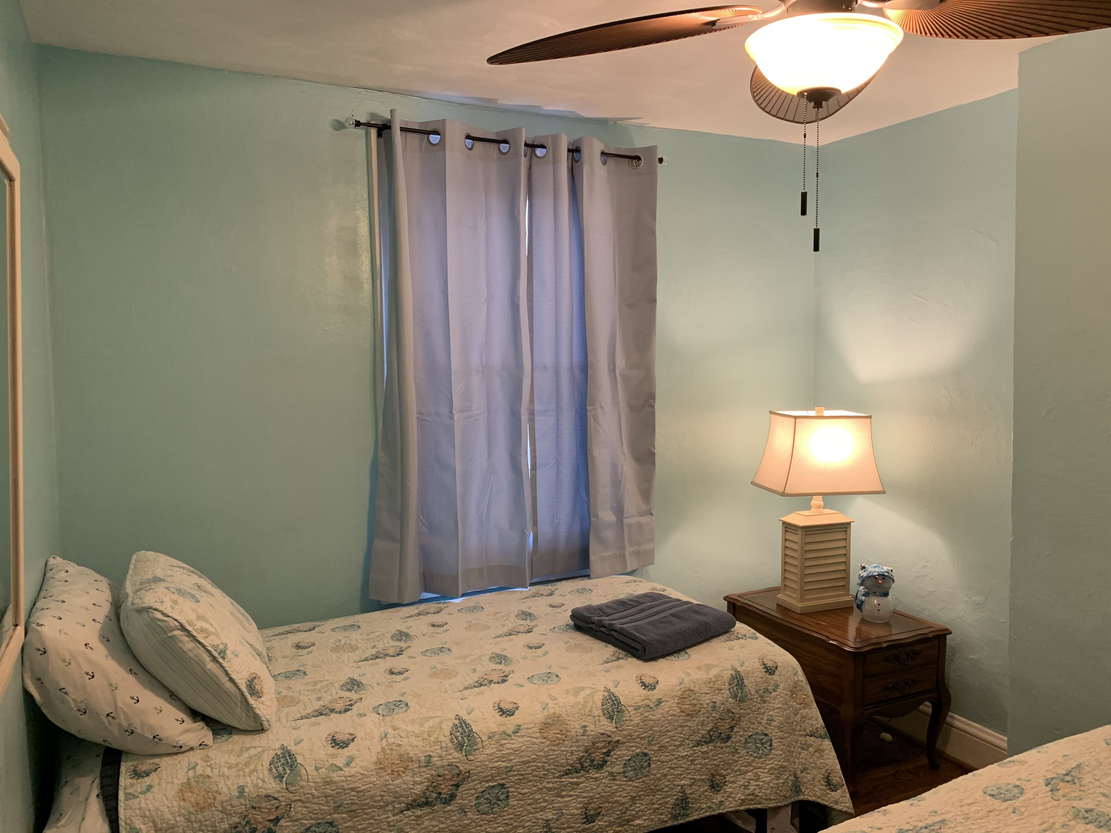 A bedroom with a bed, a nightstand, a lamp, a ceiling fan, and a window with curtains.
