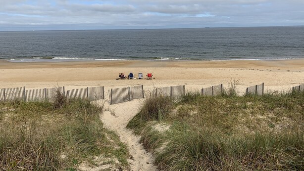 Une plage avec une clôture en bois, un sentier sablonneux et quelques chaises de plage.