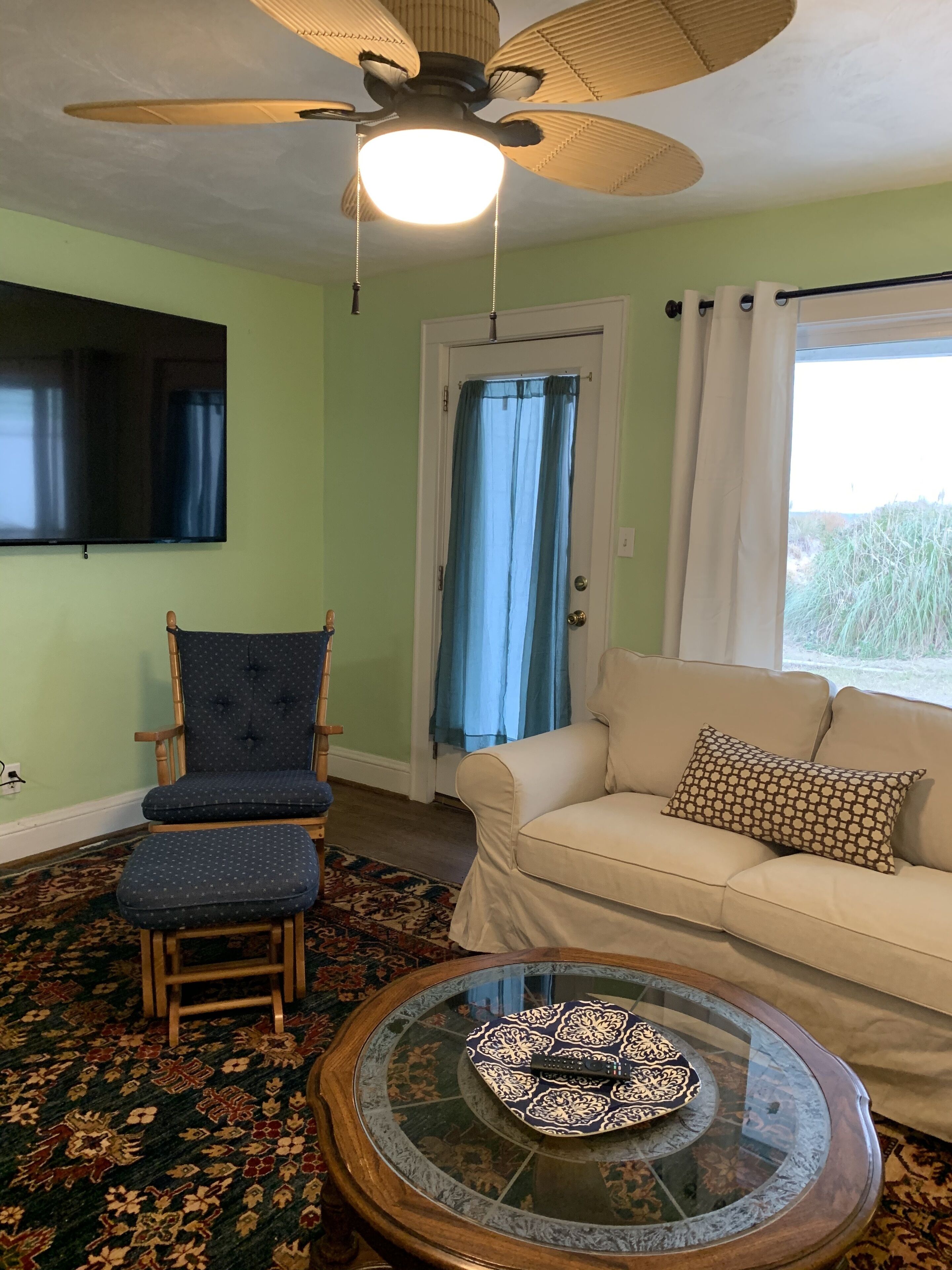 Een woonkamer met een plafondventilator, een televisie, een bank, een kamerkleed en een salontafel.