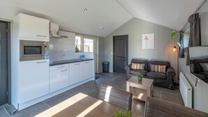 Una cocina moderna con armarios blancos y un horno empotrado, un área de comedor con mesa y sillas, y una sala de estar con sofá y televisor.
