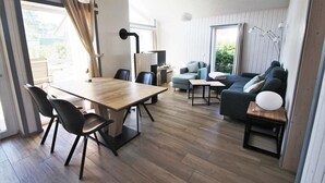 A modern living room with a wooden dining table, black chairs, a blue sofa, and a small side table with a lamp. - Ferienhaus im Skandinavischen Stil (Rechlin)