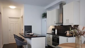 A modern kitchen with white cabinetry, a black countertop island, and a dining area with a round table. - In the Heart of Brosundet! Fully Equipped 3 Bed Room Ap (Ålesund)