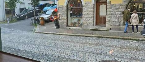 A cobblestone street with buildings, a shop with a stone facade, and a person walking.