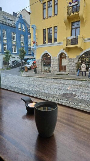 Rua de paralelepípedos com edifícios, uma loja com fachada de pedra e uma pessoa caminhando.