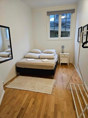 Quarto com cama, mesa de cabeceira, janela e espelho.