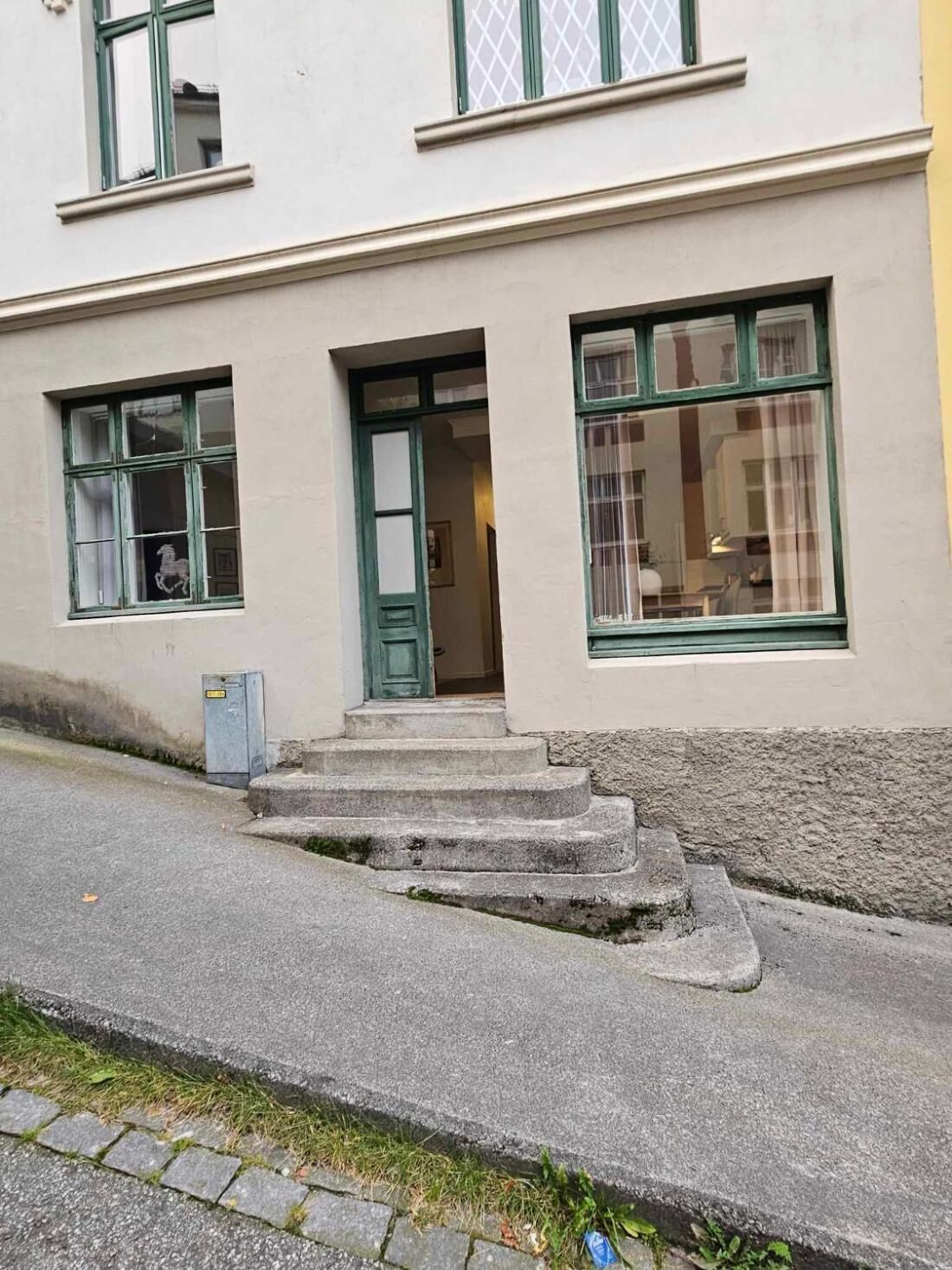 A building with a front entrance, a set of steps leading up to it, and two windows with green frames.