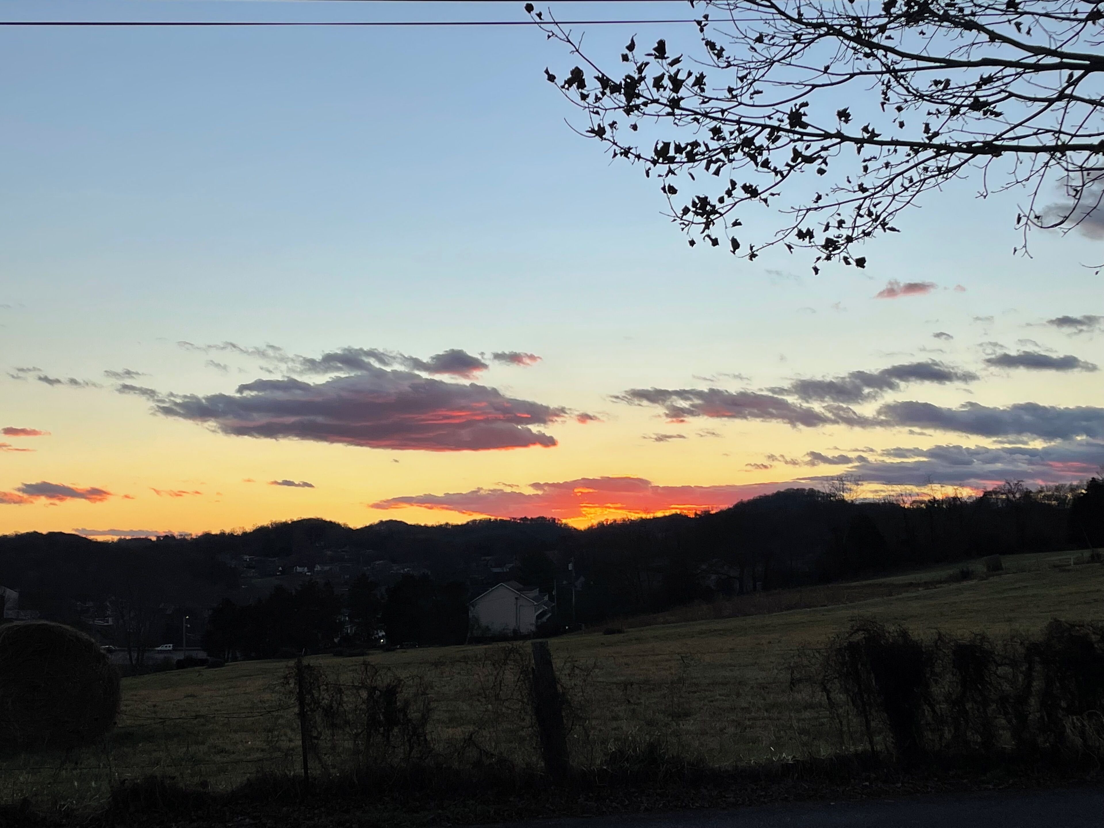 A rural landscape with a sunset, fields, and a distant building.