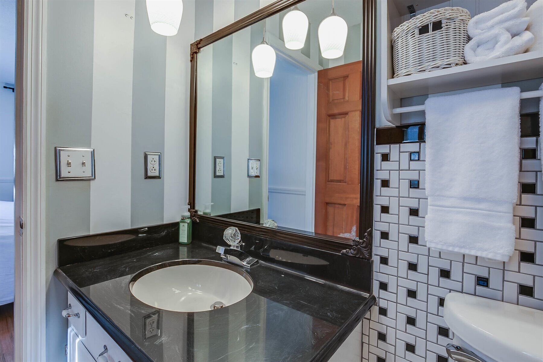 Un baño con lavamanos de mármol negro, un espejo grande y pared de azulejos.