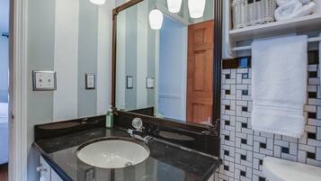 Un baño con lavamanos de mármol negro, un espejo grande y pared de azulejos.