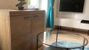 Una stanza con una scrivania in legno, un tavolino in vetro, un tappeto morbido blu e una TV appesa al muro.
