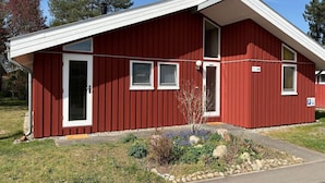 A red building with a white door, windows, and a small garden area with rocks and plants. - Ferienhaus mit Sauna im Ferienpark Mirow (Mirow)