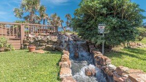 A small waterfall in a landscaped area with a wooden deck and a warning sign.