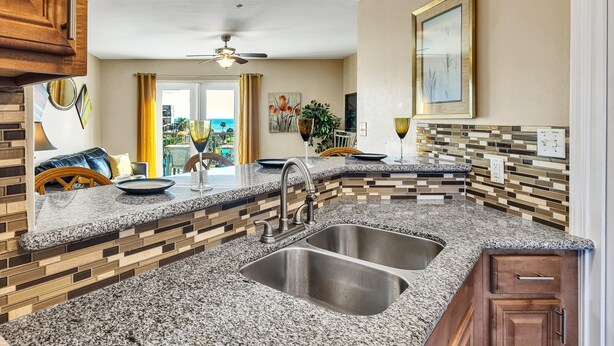 A kitchen with granite countertops, a double sink, wooden cabinets, and a view of the outdoors.