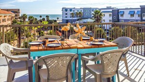 A wooden table with chairs on a balcony overlooking a beach and buildings.