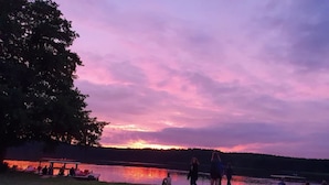Escena junto al lago al atardecer, con gente sentada y caminando cerca del agua.