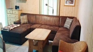 Una sala de estar con un sofá de cuero marrón, una mesa de centro de madera y un sillón de mimbre.