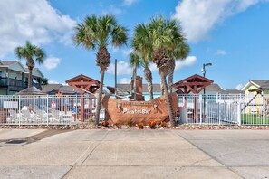 A sign with 'Pirates Bay' written on it, surrounded by palm trees and a white fence. - Spacious townhome with community pool! (Port Aransas)