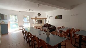 Een eetruimte met meerdere tafels en stoelen, een open haard en een klok aan de muur.