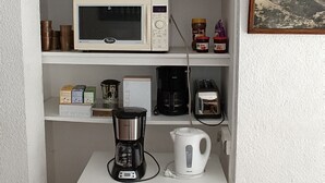 Een kitchenette met een magnetron, koffiezetapparaat en diverse keukenspullen op planken.
