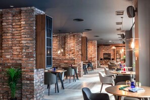 Ein modernes Restaurant mit Backsteinwänden, Holzelementen und einer Mischung aus runden und rechteckigen Tischen.