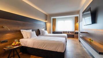 Una habitación de hotel moderna con dos camas, un televisor de pantalla plana, un cabecero de madera, una mesita con frutas y una ventana con cortinas.