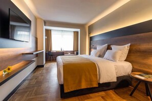Ein Hotelzimmer mit einem großen Bett, einem Schreibtisch, einem Fernseher und einem Fenster mit Vorhängen.