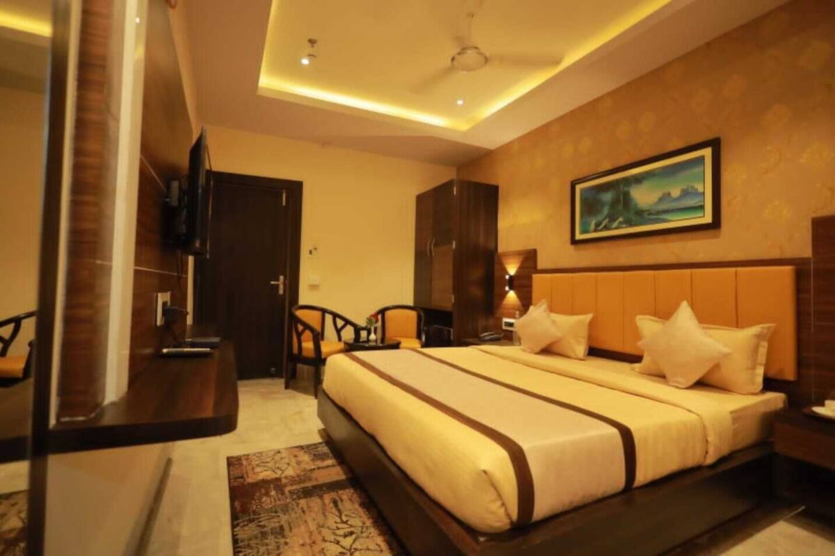 A hotel room with a large bed, a desk, a television, and a painting on the wall.