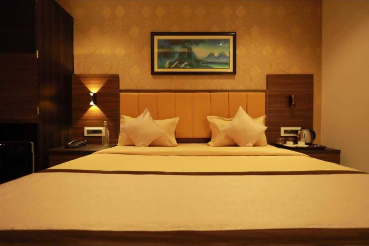 A hotel room with a large bed, two bedside tables, a nightstand, a painting on the wall, and a lamp.