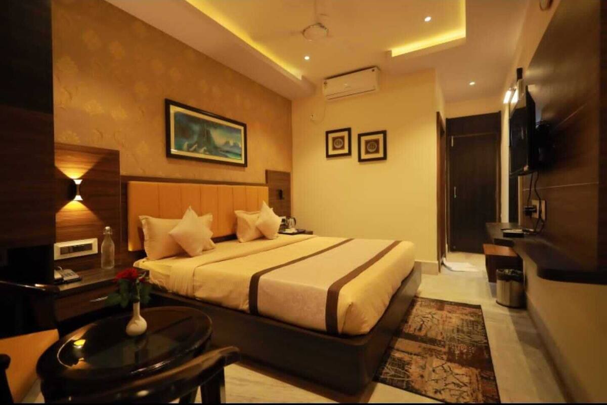 A hotel room with a large bed, bedside tables, a desk, a chair, a TV, and a painting on the wall.