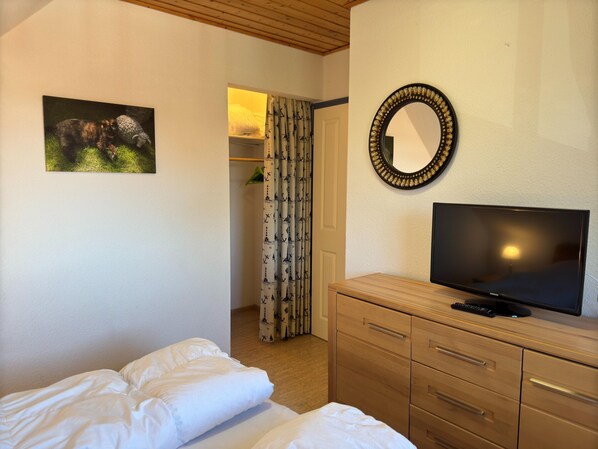 A bedroom with a bed, a TV on a wooden dresser, a mirror, and a door leading to a bathroom.