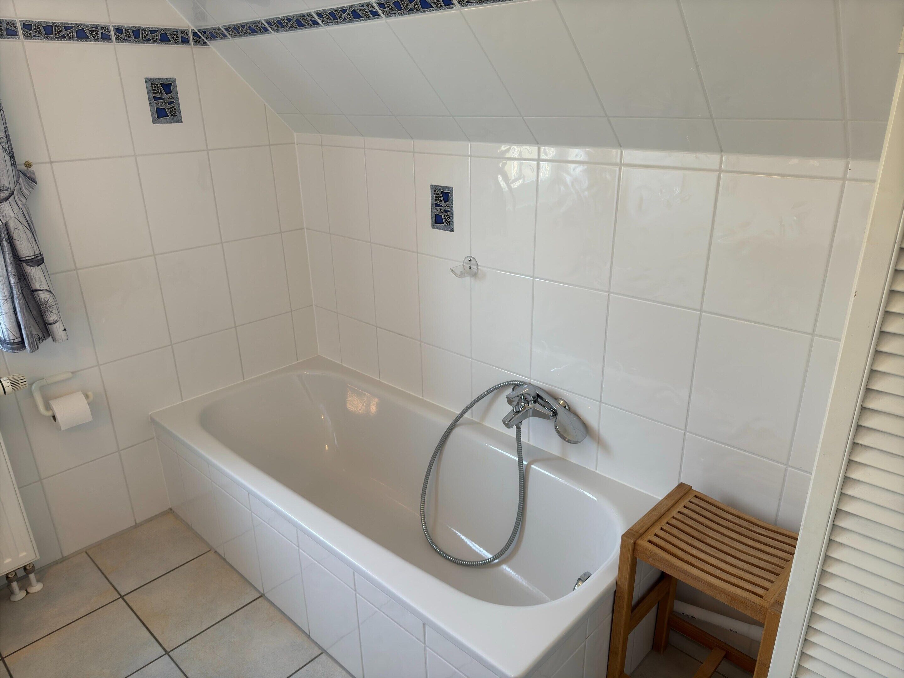 Un baño con una bañera blanca, un taburete de madera y un cabezal de ducha.