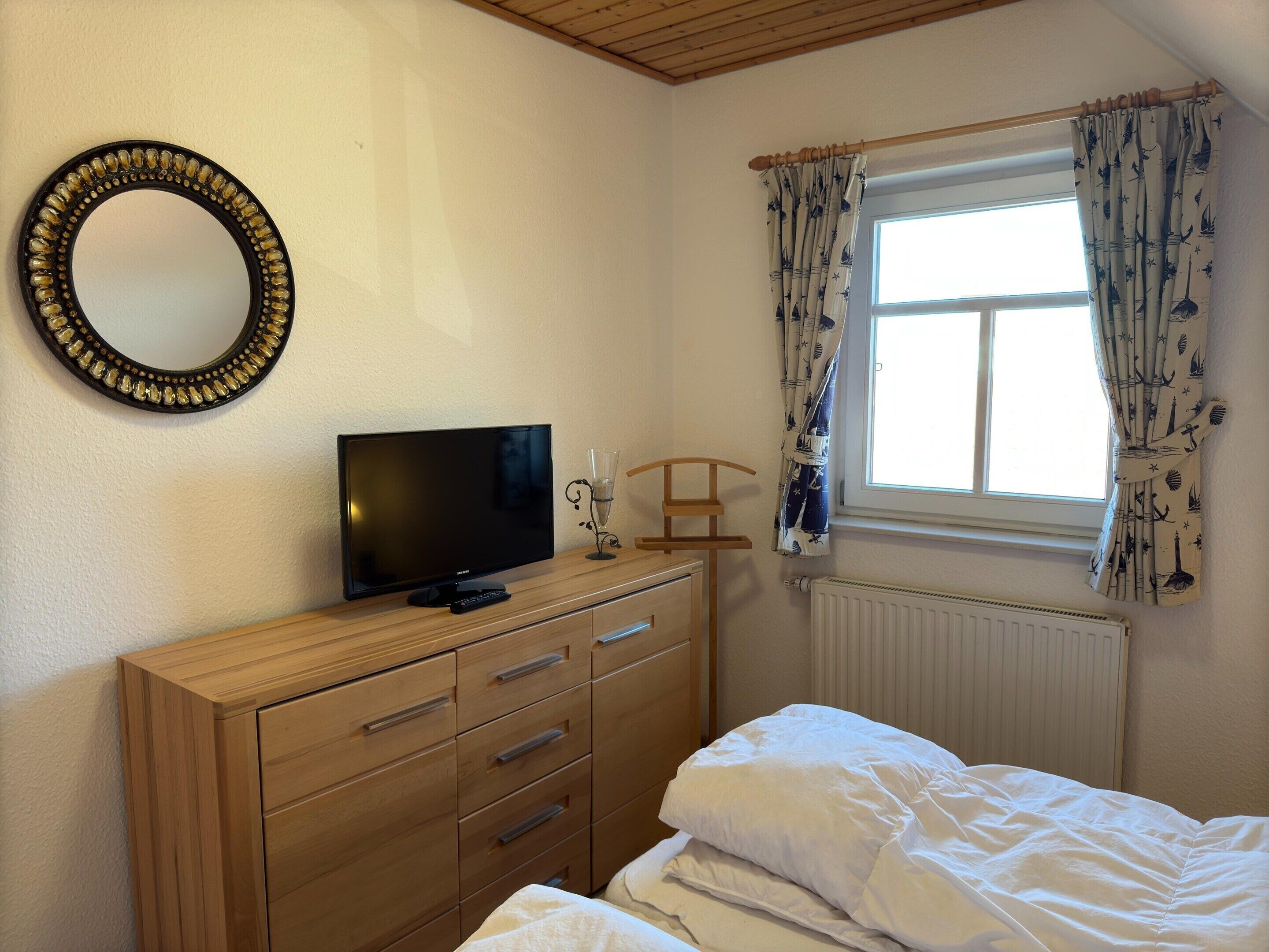 A bedroom with a wooden dresser, a television, a window with curtains, and a radiator.