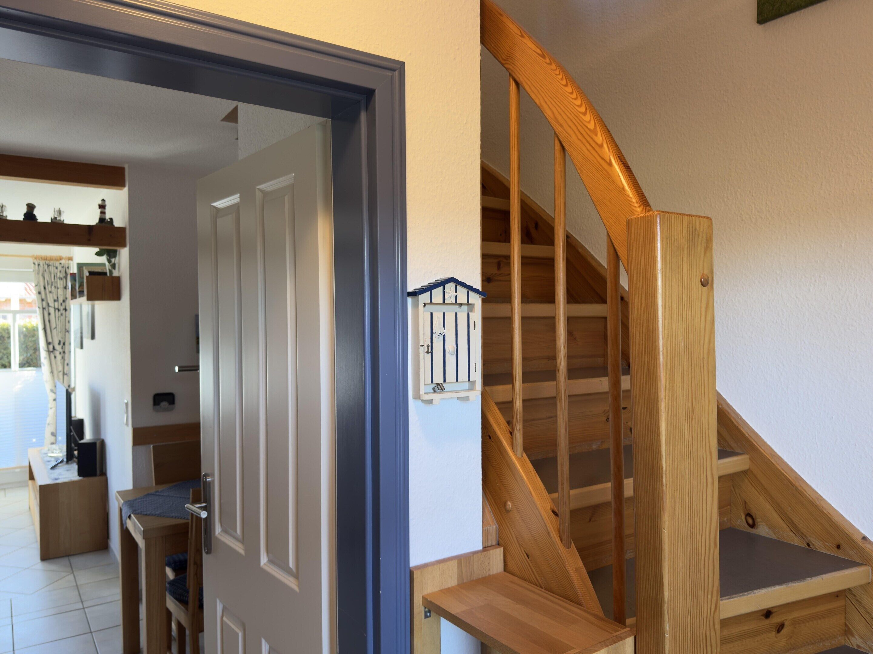 A wooden staircase with a handrail, a door leading to a room, and a small shelf with a model house.