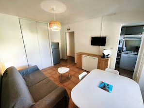 Un espace de vie compact comprenant un canapé, une table à manger, un coin cuisine et un téléviseur.