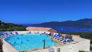 Une piscine avec des chaises bleues, une vue sur la mer et des montagnes en arrière-plan.