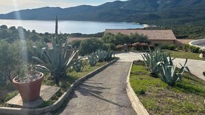 Un chemin menant à un bâtiment dont le toit est recouvert de tuiles rouges, entouré de plantes d’agave, et d’où l’on peut admirer un lac et des montagnes.
