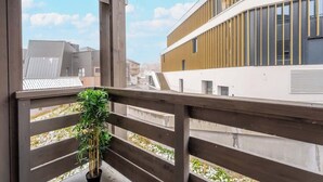 Un balcón con una planta en maceta, con vista a un edificio moderno de fachada curva y amplios ventanales.