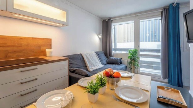 Una habitación moderna con kitchenette, una zona de comedor con mesa dispuesta para dos personas, un sofá y un televisor.
