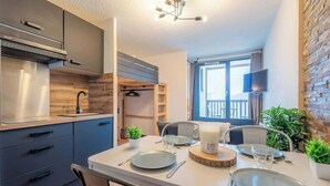 A modern kitchen with dark cabinets, a stainless steel range hood, and a dining area with a white table set for four.