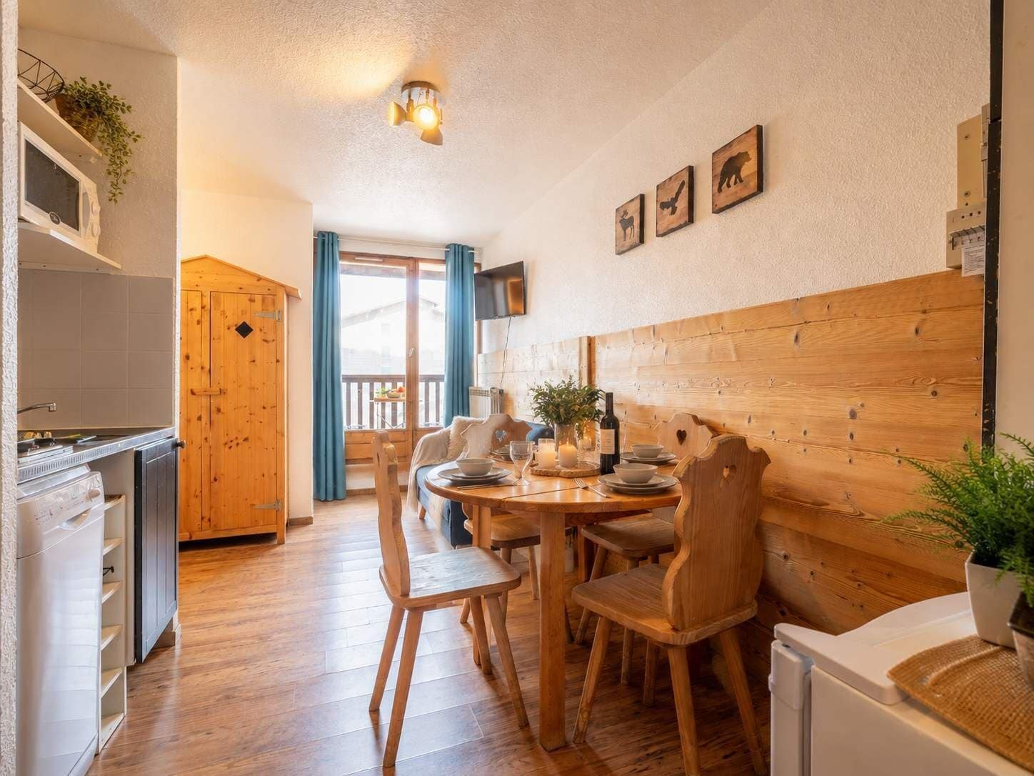 A cozy dining area with wooden furniture, a table set for two, and a view of the outdoors through a sliding door.