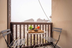 Ein Balkon mit Tisch und zwei Stühlen, einer Obstschale und einem Blumentopf.