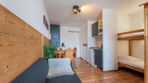 Et kompakt værelse med sengehoved i træ, sofa, køjeseng, tekøkken og spiseplads.