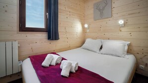 A wooden-paneled room with a bed, a window, and a wall-mounted light fixture.