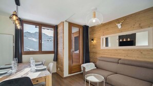 A modern interior with a wooden wall, a sofa, a dining table set, and a view of mountains.