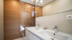 A modern bathroom with a large mirror, two sinks, and a shower area.